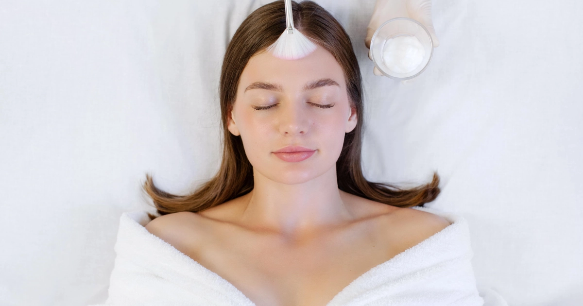 A woman on a treatment bed receiving a Chemical Peels treatment in Brooklyn, NY with a facial mask applied using a brush