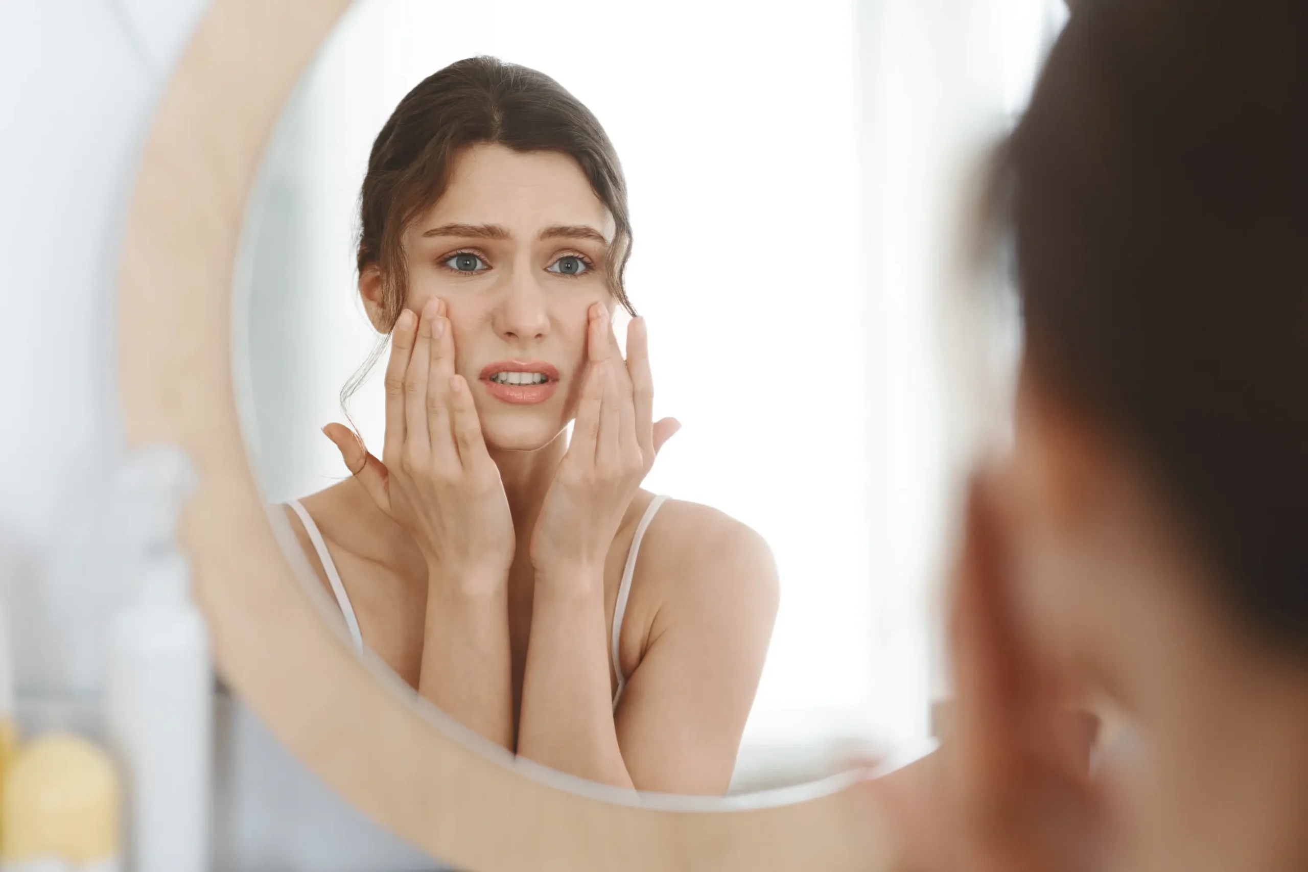 A worried woman touching her face looking in the mirror in Brooklyn, NY | Mrs. Webb Aesthetic
